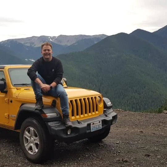 A picture of Chris Saganic sat on a Jeep in the mountains